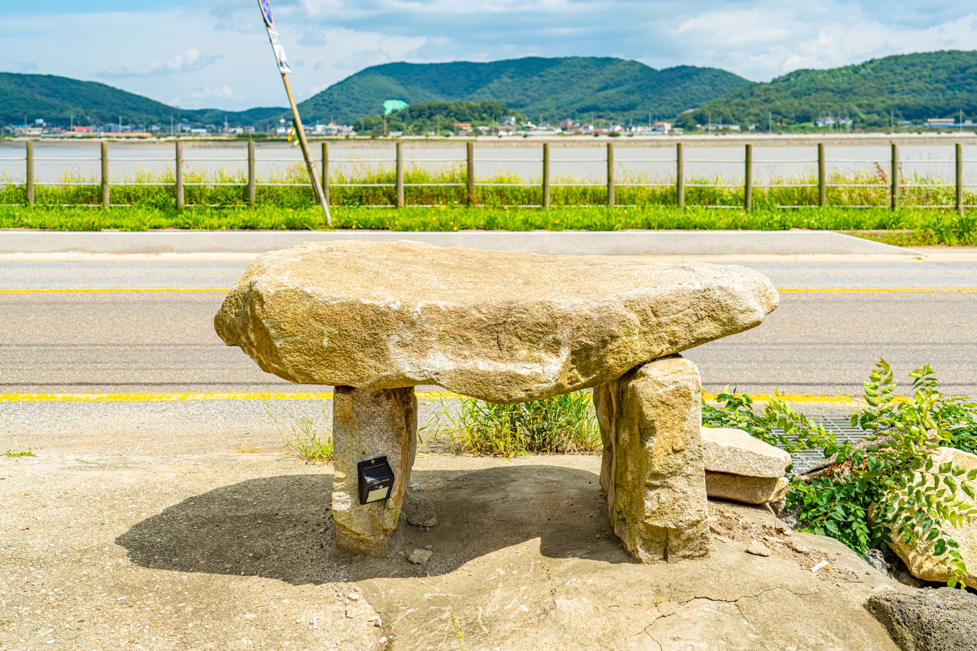 해안도로 옆에 놓인 작은 고인돌 조형물, 그 너머로 강화해협과 초록 언덕이 보입니다 (임시 사진)