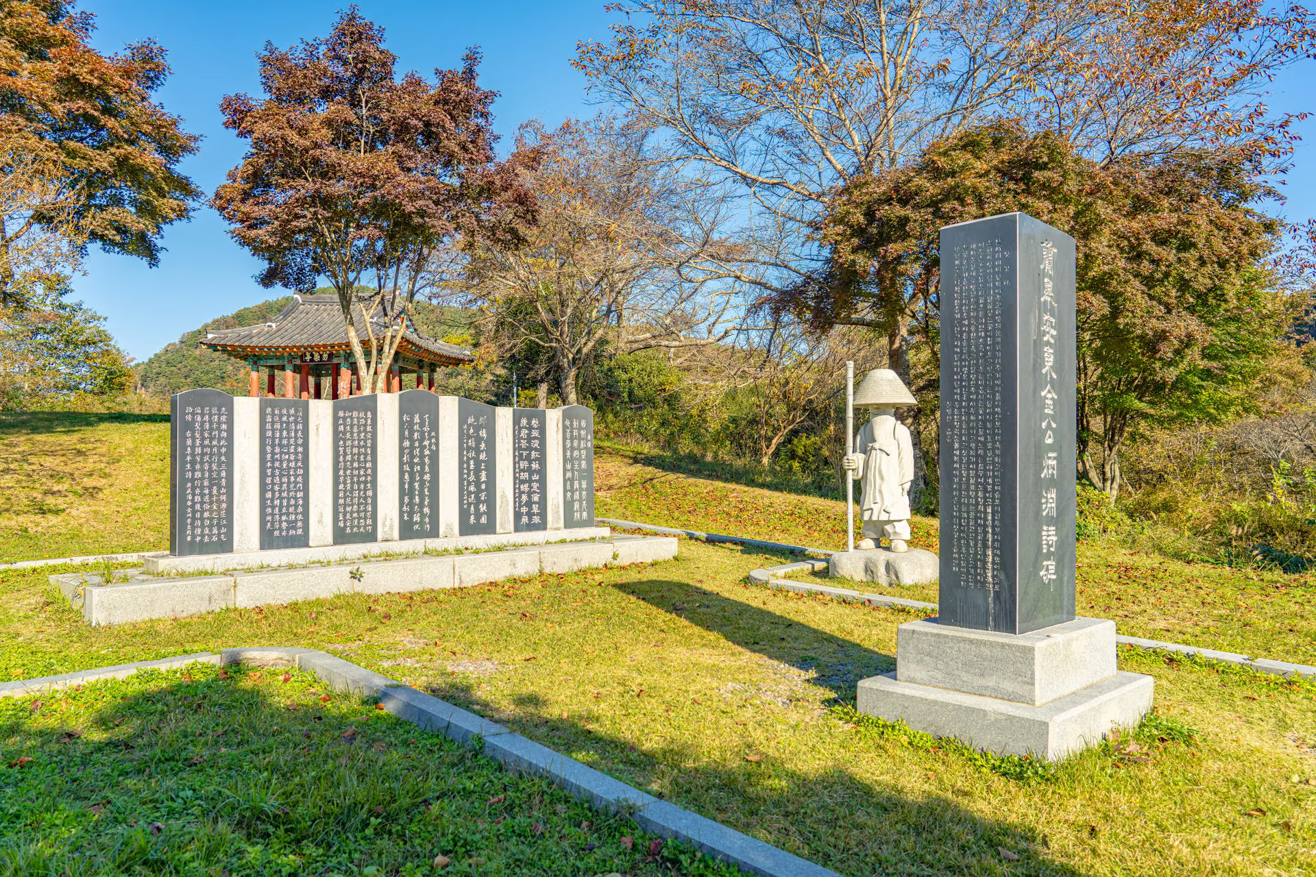 ‘蘭皐安東金公炳淵詩碑’라 새긴 비와 삿갓 쓴 석상, 뒤로 한 줄로 선 돌판. 단풍 든 나무 너머로 물염정 지붕이 보인다