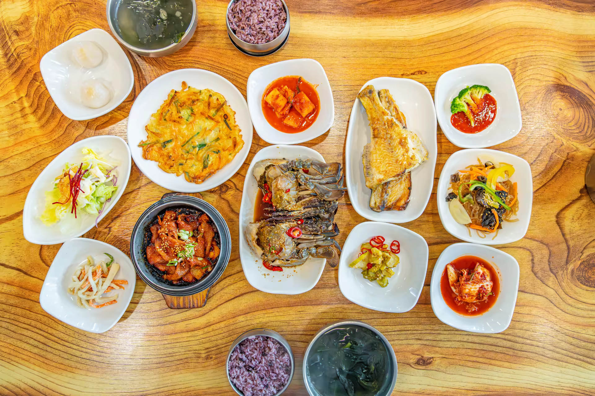 나무 식탁 위에 간장게장과 생선구이, 김치찌개, 김치전, 나물 반찬이 가득 차려진 인천 간장게장 백반 한 상