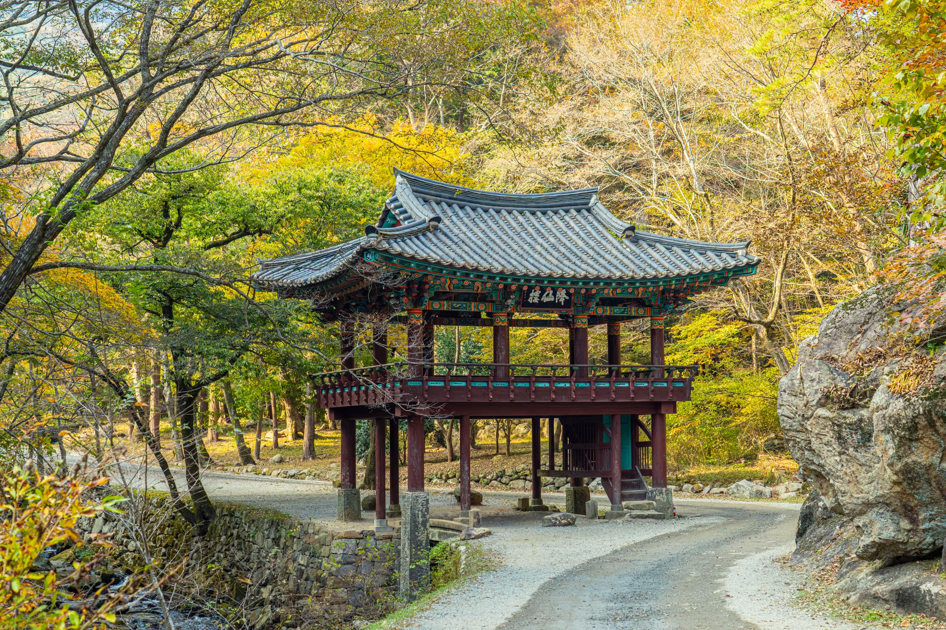 단풍 든 활엽수 숲과 큰 바위 사이, 굽은 길 위에 선 2층 누각 강선루
